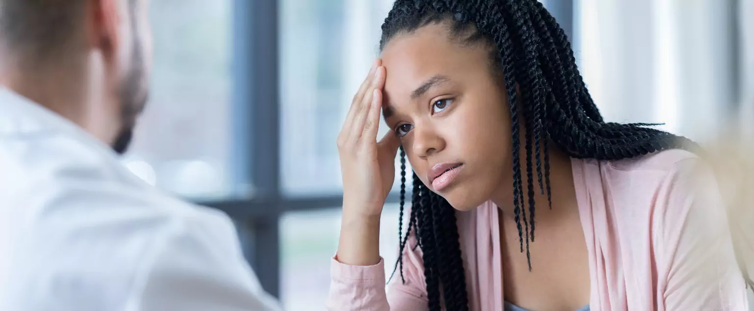 Teen girl with hand on forehead talking to a doctor