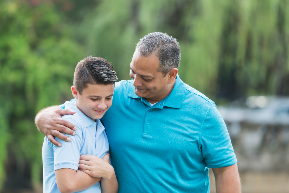 Father puts arm around teen son as they walk and talk together outside.