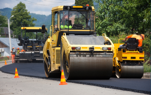 A yellow paving roller drives over freshly laid asphalt on a road.